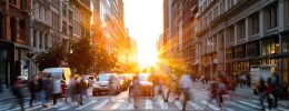 Crowds of busy people walking through the intersection of 5th Avenue and 23rd Street in Manhattan, New York City with bright sunset background