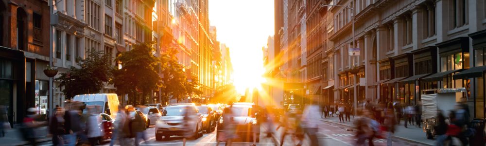 Crowds of busy people walking through the intersection of 5th Avenue and 23rd Street in Manhattan, New York City with bright sunset background